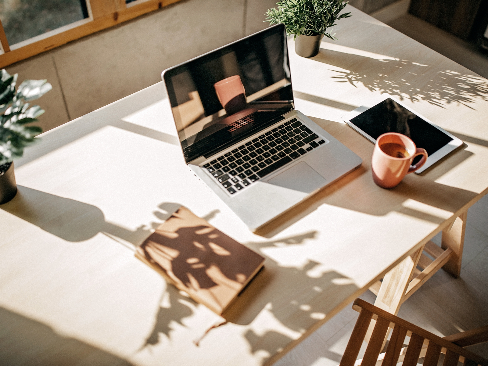Sunlit workspace with a laptop, notebook, tablet and coffee cup.